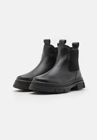 Botas de tobillo negras de cuero con un acabado suave, paneles laterales elásticos y suelas de goma texturizadas; cuentan con lengüetas para facilitar el calzado.