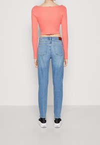 Korallfärgad kortärmad topp med scallopkant i nederkant, kombinerad med ljusblå smala jeans. Har två bakfickor och svarta skor.