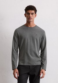 Graues langärmliges T-Shirt aus weichem Material mit Rundhalsausschnitt. Verfügt über ein minimalistisches Logo auf der Brust und eine lockere Passform.