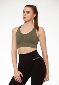 Top sportivo verde oliva con davanti arricciato, abbinato a leggings neri a vita alta con il nome del marchio "STARK SOUL" in bianco.