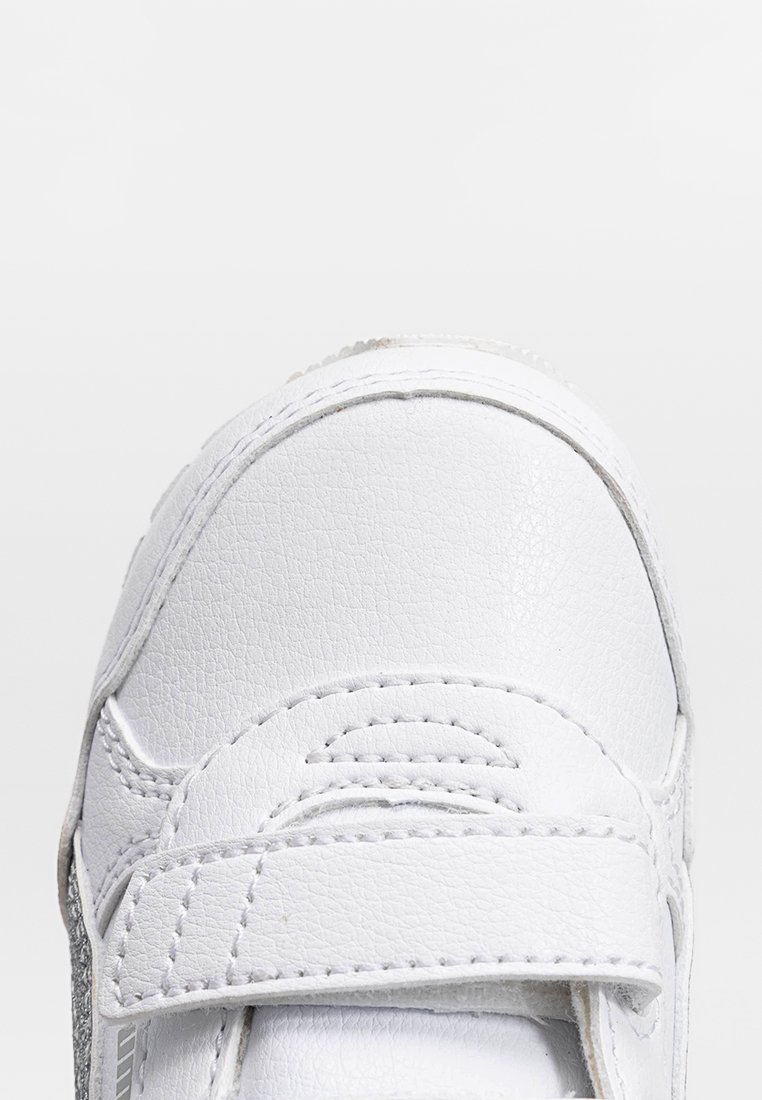 Sneaker bianca in pelle con punta testurizzata, fissata da una fascia in velcro, caratterizzata da cuciture sottili e un pannello laterale grigio.