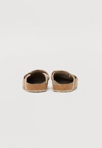 Sandales en liège marron avec dos ouvert, dessus texturé et semelle en caoutchouc robuste. Design minimal avec des coutures discrètes et une sangle ajustable.