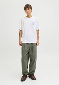 Balts kokvilnas T krekls ar brīvu piegriezumu, ar mazu krāsainu grafiku kreisajā krūtī. Olīvu zaļa platā kāju bikses un tumši brūnas kurpes.