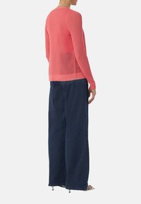 Rosa, leichter Strickpullover mit lockerer Passform, gerippter Textur und langen Ärmeln, kombiniert mit dunkelblauen weit geschnittenen Jeans.