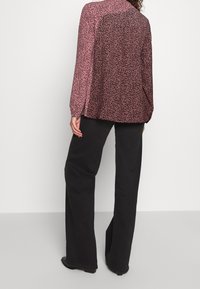 Blouse à imprimé léopard rose avec manches longues, coupe décontractée et détails de boutons aux poignets, associée à un pantalon noir à jambes larges.