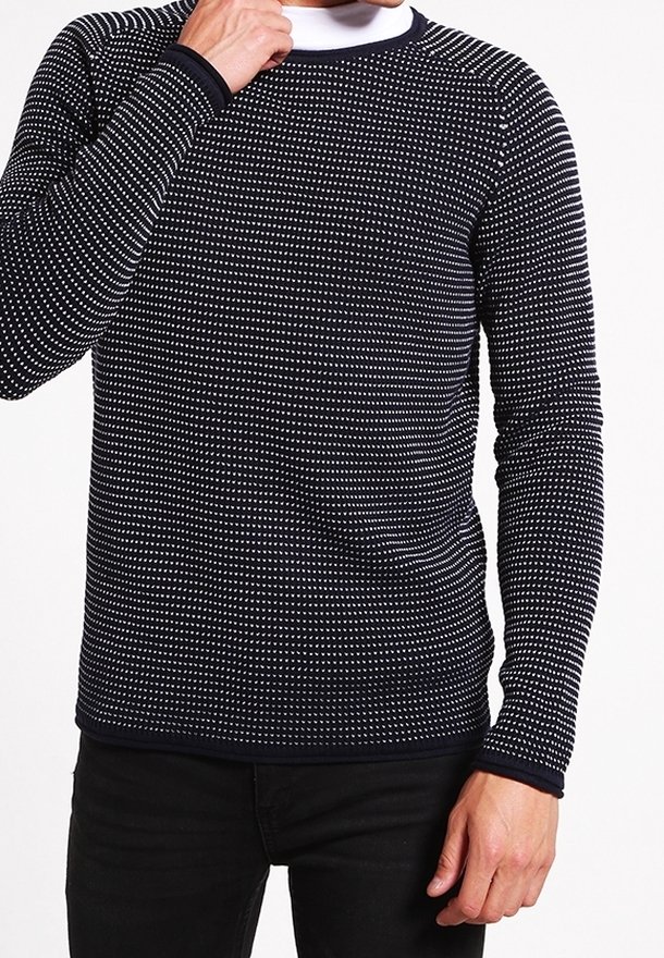 Pull à manches longues bleu marine avec motif à pois blancs, col rond et poignets côtelés. Le tissu semble tricoté, offrant une finition texturée.