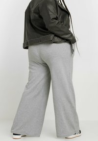 Grå, vida sweatpants gjorda av mjukt, texturerat tyg; kombinerat med en svart läderjacka och svart-vita sneakers.