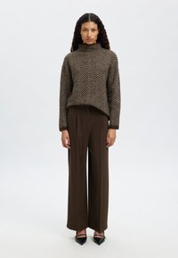 Rjavi pulover iz žamete z ribjo kosti in z visokim ovratnikom, kombiniran s širokimi hlačami temno rjave barve ter črnimi čevlji s koničastim sprednjim delom. Povsod gladke teksture.