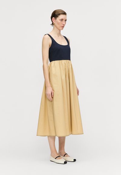 Niebieska sukienka tank top z marszczoną beżową spódnicą do połowy łydki, gładką tkaniną, bocznymi kieszeniami oraz płaskimi butami z czarną lamówką.