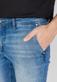 Jeans de mezclilla azul desgastados con un corte ajustado, que presentan un diseño de cinco bolsillos, cierre de botón metálico y detalles de costura visibles.