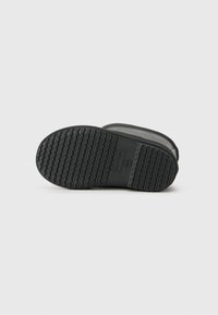 Semelle extérieure en caoutchouc noir avec motif de grip texturé, arborant une pièce grise marquée. Bords lisses et arrondis avec un design général minimal.