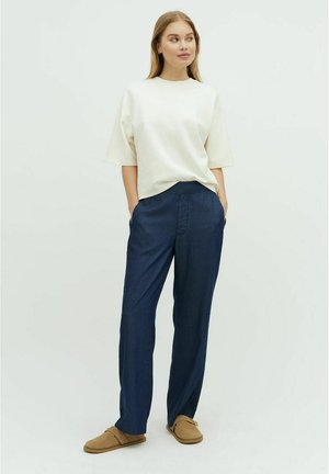 Tricou oversized de culoare crem deschis, cu mâneci scurte, asortat cu pantaloni largi de culoare albastră închisă. Modelul poartă papuci de culoare bej. Stil simplu și casual.