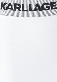 Hvit elastisk stoff med en teksturert midjebånd som har svart "KARL LAGERFELD" bokstaver. Jevn overflate med lett glans.