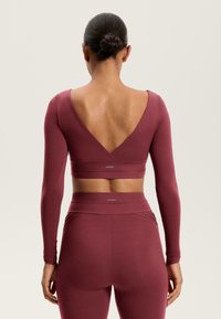 Hosszú ujjú, mély V-hátú crop top és magas derekú leggingsek sötét bordó színben, rugalmas anyagból, sima textúrával.