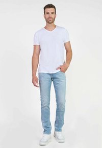 Camiseta de algodón blanca de cuello en V, vaqueros slim-fit de color azul claro y zapatillas blancas. Diseño simple sin patrones o acentos visibles.