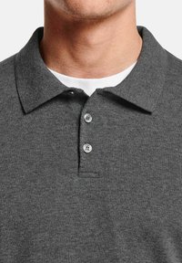 Polo gris charbon avec un col classique, deux boutons brillants et un tissu tricoté texturé. Superposé à un t-shirt blanc à col rond.