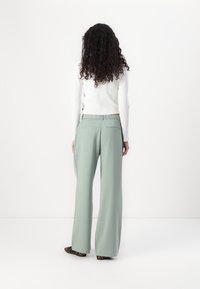 Pantalons larges vert clair en tissu lisse, avec une taille ajustée, deux poches arrière et un design subtil et ajusté.
