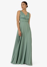 Lange, vloerlange jurk inMuted mintgroen met een kanten lijfje, V-halslijn en vloeiend materiaal voor een zachte, elegante silhouet.