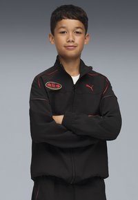 Svart zip-up-jacka med röda detaljer och logotypmärke, med hög krage och elastiska muddar, kombinerad med matchande byxor.