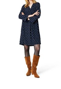 Granatowa sukienka w złote kropki, z dekoltem w kształcie litery V i długimi rękawami; połączona z brązowymi zamszowymi botkami do kolan.