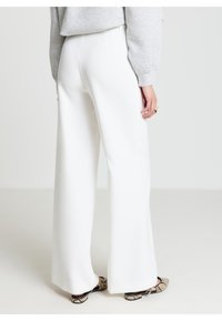 Pantaloni bianchi a gamba larga realizzati in tessuto liscio, caratterizzati da vita alta e design minimalista, abbinati a scarpe con stampa animalier di serpente.