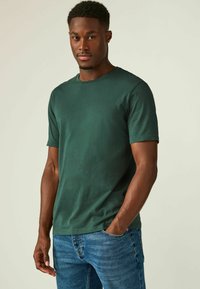 Grøn bomulds T-shirt med korte ærmer og rund halsudskæring, der har en glat tekstur og standard pasform. Båret med blå jeans.