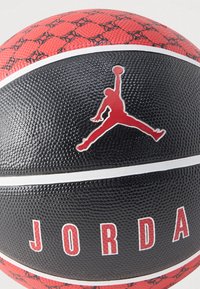 Piros és fekete kosárlabda, amelyen a Jumpman logó és a „JORDAN” szó vastag piros betűkkel jelenik meg a texturált panelek között.