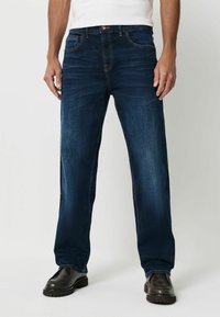 Tmavě modré džíny s rovnými nohavicemi, zdobené oranžovým prošíváním, pěti kapsami a knoflíkovým zapínáním. Texturovaná látka dotváří vzhled.
