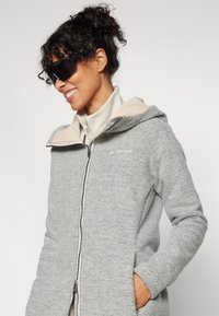 Gray zip-up jacket with a beige hood lining and collar. Features a smooth texture, long sleeves, and a logo on the chest.
