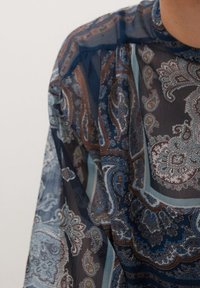 Blouse transparente bleu marine avec motif cachemire, présentant des dessins complexes en turquoise, marron et argenté. Texture douce avec tissu léger.