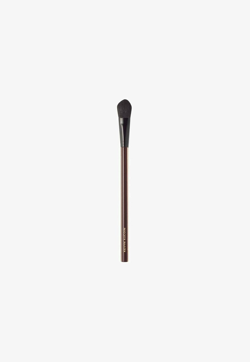 Makeup brush with a tapered, rounded head; soft bristles in black; a slim, metallic bronze handle; engraved lettering near the base.