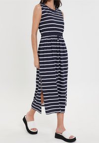 Robe maxi rayée bleu marine et blanche avec un design sans manches, taille froncée, fentes latérales, et associée à des sandales compensées noir et blanc.