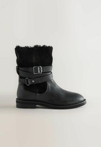 Stivale alla caviglia in pelle nera con parte superiore in suede, alamaro largo e fibbia decorativa. Suola piatta e punta arrotondata. Accenti testurizzati nella parte superiore.