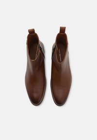 Hnědé kožené kotníkov�é boty s hladkým povrchem, špičatou špičkou, zipem na boku a poutkem na zadní straně.