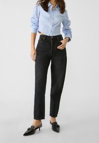 Jeans negros de cintura alta con un corte recto, combinados con una camisa de botones a rayas azul claro y zapatos de tacón negro de punta.