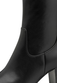 Stivaletto in pelle nera con texture liscia, dotato di una cucitura evidenziata e di un dettaglio a taglio curvo lungo il lato. Tacco impilato.