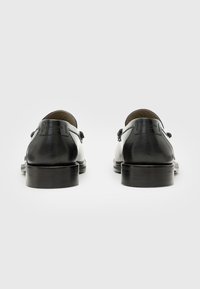 Black leather dress shoes with a smooth finish, rounded toe, and minimal detailing, featuring a low stacked heel and subtle logo on the back.
