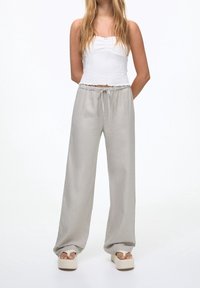 Pantalons en lin gris clair, amples, avec une taille élastique et un cordon de serrage. Associés à un crop top texturé blanc et des sandales à plateforme.