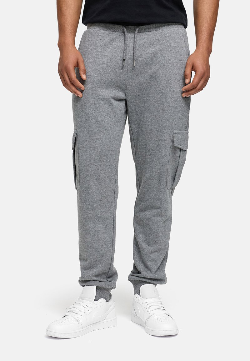 Pantalons de jogging gris en mélange de coton doux, dotés de poches cargo sur les côtés, de poignets élastiques et d'une taille avec cordon de serrage, associés à des baskets blanches.