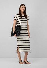 Gestreiftes Strickoberteil und Rock in Creme und Schwarz, mit lockerer Passform, Seitenschlitzen, und kombiniert mit einer strukturierten schwarzen Tasche und flachen Sandalen.