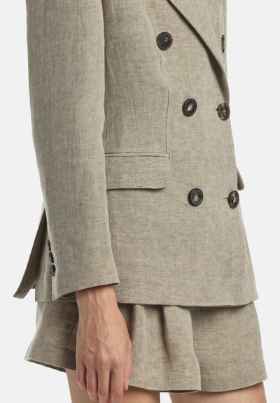 Beige színű, dupla soros vászon blézer hat kontrasztos gombbal és oldalzsebekkel, hozzáillő, bővülő szabású miniszoknyával párosítva.