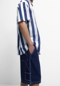 Koszulka w paski z krótkim rękawem w kolorze granatowym i białym, zestawiona z niebieskimi szortami dżinsowymi z kieszeniami i kontrastowym przeszyciem.