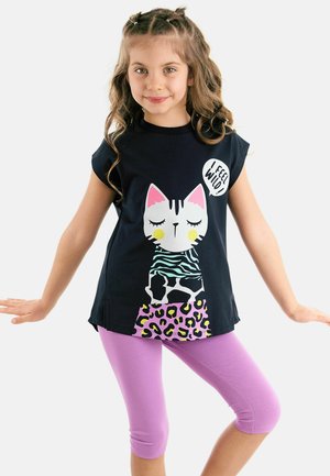 Schwarzes T-Shirt mit kurzen Ärmeln und einem Cartoon-Katzen-Graphic in Weiß, Grün und Pink, kombiniert mit lila Capri-Leggings. Gemusterte Akzente auf dem Shirt.