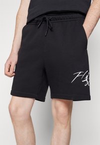 Černé bavlněné kraťasy s elastickým pasem a šnůrkou; obsahují bílé grafické detaily na dolní části nohy; délka ke kolenům.