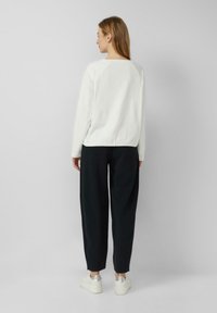 Witte trui met een ronde hals en raglanmouwen, gecombineerd met zwarte, loszittende broek en witte sneakers met zilveren accenten.