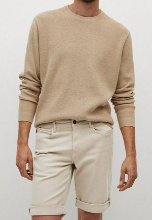 Beige strukturierter Strickpullover mit langen Ärmeln, kombiniert mit hellen hochgekrempelten Shorts. Einfaches Design, ohne sichtbare Muster oder Hardware.