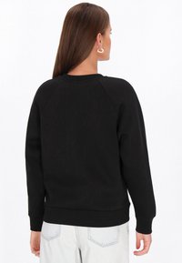 Czarna bluza z prążkowanym dekoltem typu crew oraz raglanowymi rękawami. Materiał jest gładki; ma luźny krój oraz elastyczne mankiety i dół.