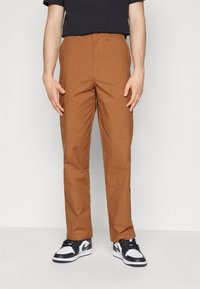 Bruna cargobyxor tillverkade av slitstarkt tyg, med sidofickor, en rak bendesign, och matchade med svarta och vita sneakers.