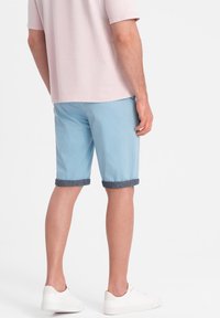 Světlé modré šortky s denimovými obroučkami, vyrobené z hladkého materiálu. Nošeny s růžovým tričkem s krátkým rukávem a bílými teniskami.