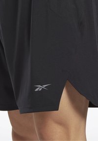 Svarta träningsshorts i lätt material, med en grå logotyp på det nedre benet och en sidoklyvning för förbättrad rörlighet.